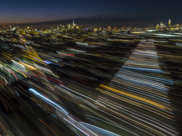 纽约布鲁克林布什维克的高架地铁和默特尔大道的鸟瞰图，从远处可以看到曼哈顿在夜晚的灯光。长时间曝光拍摄。图片下载