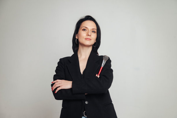 肖像自信时尚的成年妇女化妆刷在灰色的墙背景，看着相机。女商人化妆艺术家在工作室摆姿势。时尚，时尚，经营理念。本空间图片下载