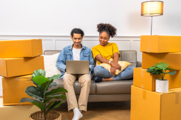 年轻的男女夫妇在搬到新公寓打开箱子时坐在地板上拥抱，看起来很满意。图片下载