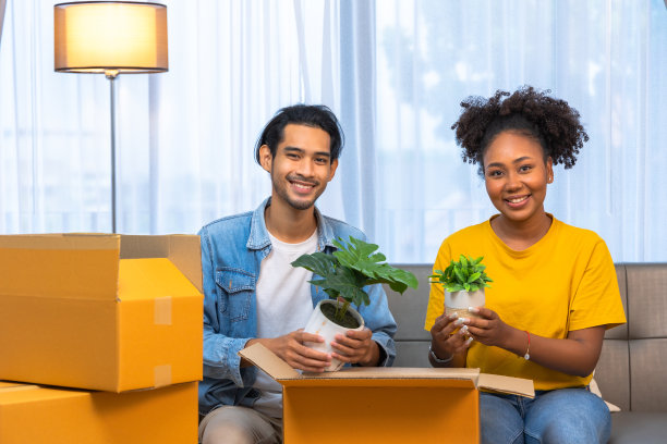 年轻的男女夫妇在搬到新公寓打开箱子时坐在地板上拥抱，看起来很满意。图片下载