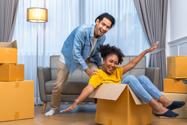 年轻的男女夫妇在搬到新公寓打开箱子时坐在地板上拥抱，看起来很满意。图片下载