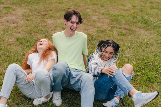 快乐年轻的三个好朋友在户外坐在公共公园的草地上玩得很开心。女性友谊的概念。友善的概念，支持人们与多元化的乐趣，千禧年的z世代。图片下载