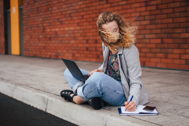 年轻的女学生坐在外面的地板上，用笔记本电脑写笔记。使用电脑。享受自由职业远程工作或远程教育图片下载