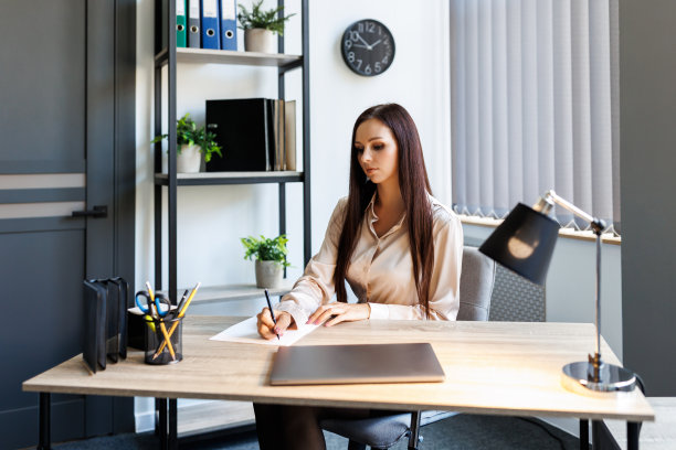 一位年轻漂亮的女士正在办公室的办公场所处理文件。一位女士坐在办公桌前签署文件图片下载