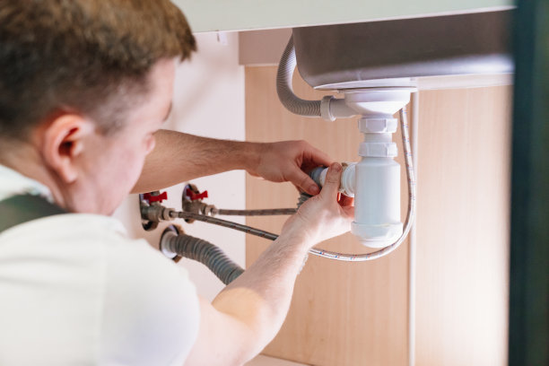 一名男水管工正在修理浴室水槽下的虹吸。图片下载