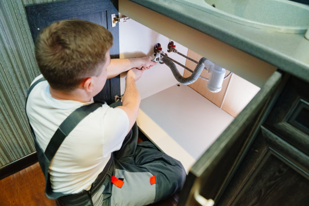 一名男水管工正在修理浴室水槽下的虹吸。图片下载