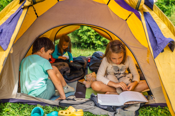 小孩子，小孩子在橙色的旅游帐篷里玩耍，看书。家庭旅行，远足大自然。后院游戏，玩得很开心。户外休闲活动。自组装，在草坪、草地上搭建露营帐篷图片下载