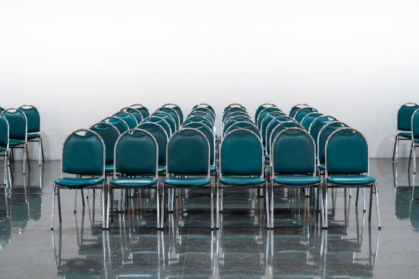 一间宽敞的大厅里有许多空的绿色皮椅子，灯还亮着。地板反射物体。给人一种空虚的感觉。图片下载