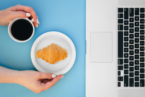 羊角面包，一杯咖啡，蓝色背景的笔记本电脑，平躺着。图片下载