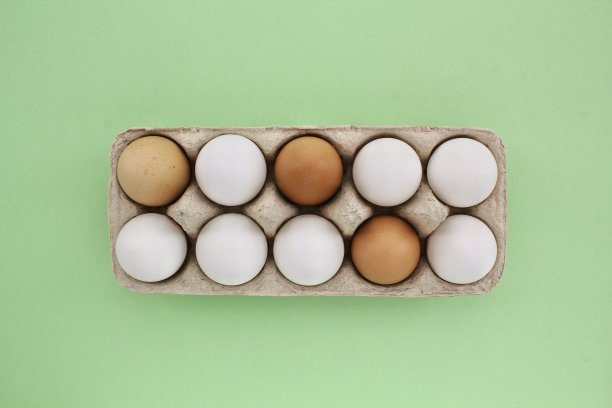 新鲜的白棕色鸡蛋装在绿色背景的纸盒里。天然健康营养有机农场食品产品理念图片下载