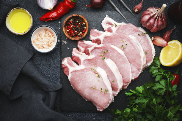 生猪排，用大蒜、百里香、香料和胡椒粉放在石板上烹调的肉。黑色厨房桌子，俯视图图片下载