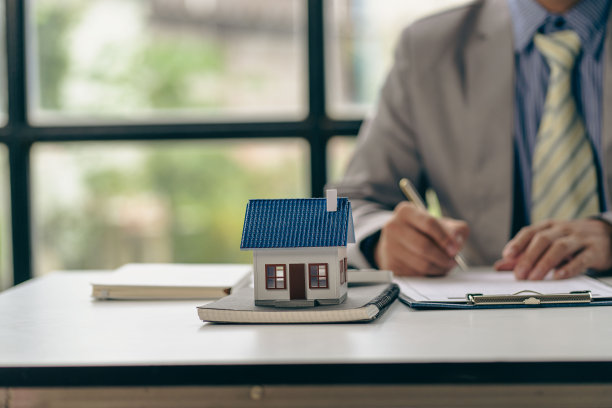 房地产办公室，销售代表坐在一张桌子前，桌上放着合同文件和一台笔记本电脑，旁边是一栋小房子。图片下载