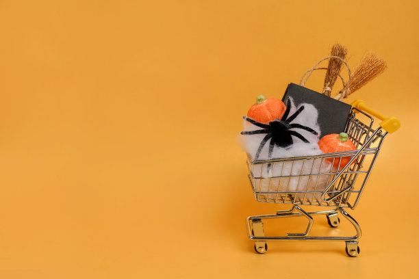 万圣节的购物车与纸袋，蜘蛛和南瓜在橙色的背景，复制空间图片下载