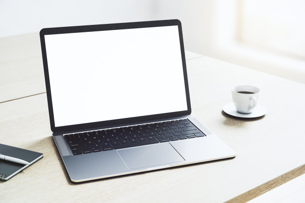 视角空白白色现代笔记本电脑显示器与您的标志或文字的拷贝空间轻木桌咖啡杯在阳光充足的办公区域。3D渲染，模拟图片下载