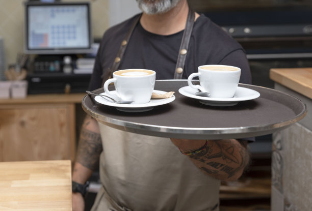 咖啡服务员:在咖啡店或酒吧里端着盛有咖啡的托盘工作的服务员图片下载