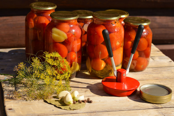 木桌上放着玻璃罐子，里面装着铁盖的番茄罐头，还有大蒜、莳萝、铁盖和一台缝衣机。家庭储存解决方案，保存剩菜，罐装概念，乡村组成图片下载