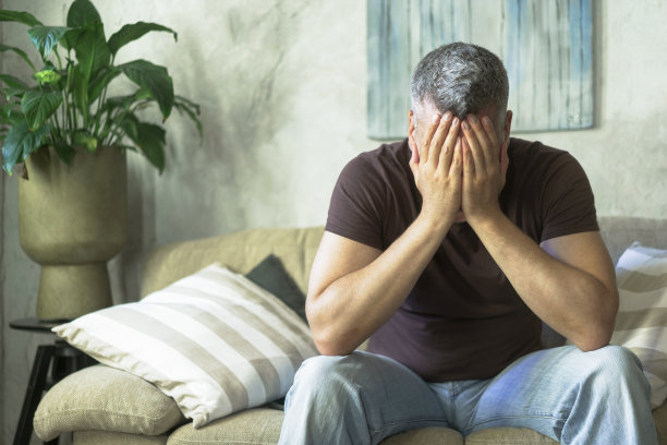 疲惫的中年白发男子坐在家里的沙发上用手捂着脸。缺乏灵感的悲哀人。中年男子危机观念。家庭危机，悲人在家图片下载