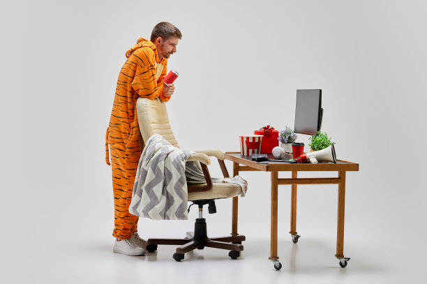 年轻男子穿着神奇的老虎服装坐在家里的电脑桌前。艺术，想法，创造力，工作和假期的概念图片下载