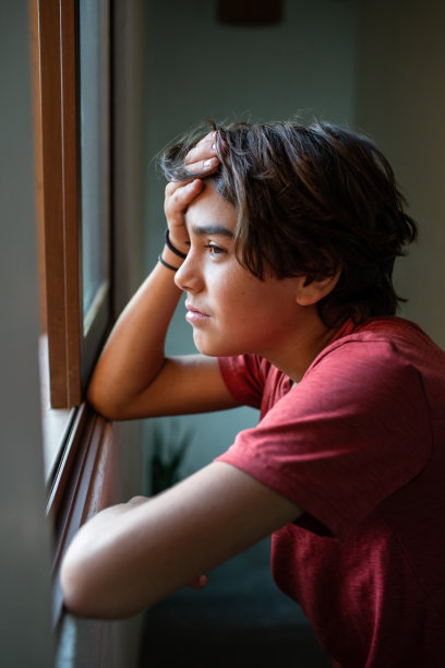 悲伤，忧虑的青春期前男孩望着窗外图片下载