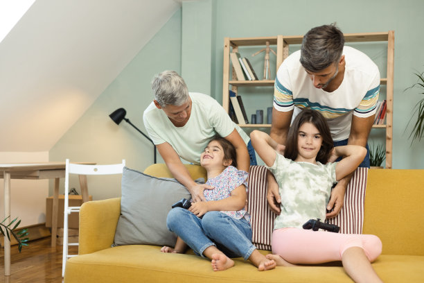 父母在两个女儿玩电子游戏时给她们挠痒痒图片下载