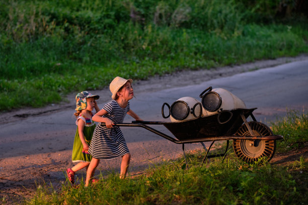 在一个公共有机花园里，一个小女孩用手推车搬运木桶，去收集河水灌溉他们的田地图片下载