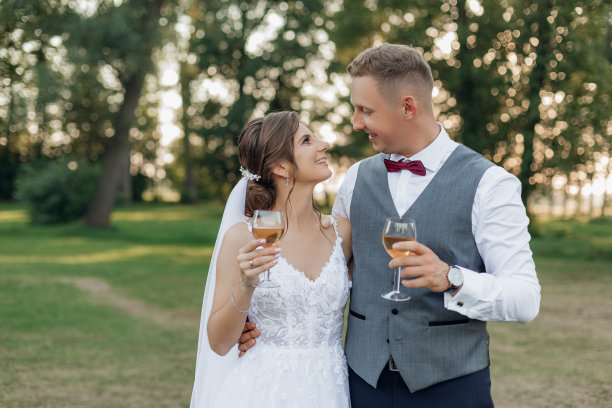 年轻的新郎拥抱年轻的新娘，手持酒杯，相遇的眼神。关系,婚礼,庆典。图片下载