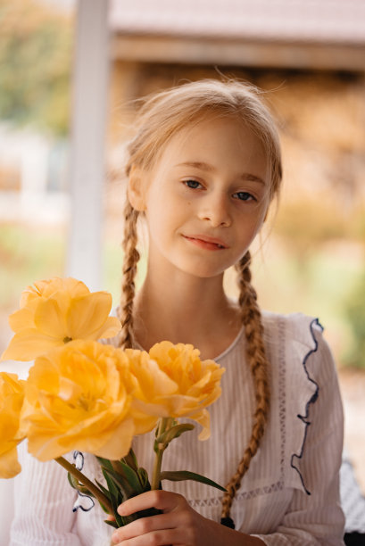 一个扎着小辫子的女孩嗅着黄色的郁金香。美丽的春天照片，一个女孩扎着辫子。手捧鲜花的小女孩图片下载