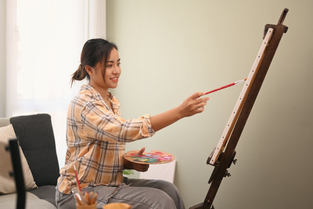 满意的女画家在舒适的车间用水彩画架上绘画。休闲活动、创作爱好和艺术观念。图片下载