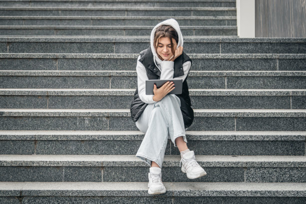 一名年轻的女学生站在外面，手里拿着一块平板电脑。图片下载