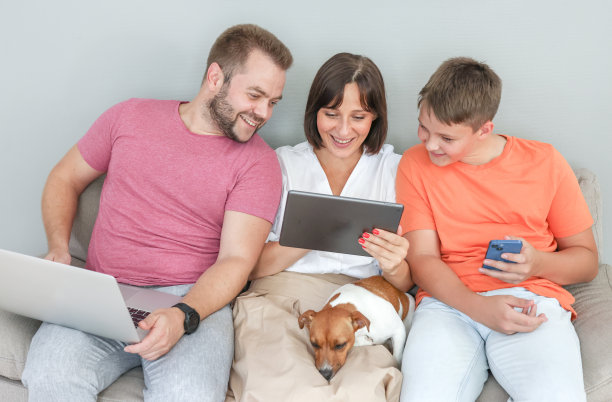 一家人正兴致勃勃地一起看平板电脑上的东西。爸爸妈妈和儿子坐在家里的沙发上，开心地看着平板电脑上的东西图片下载