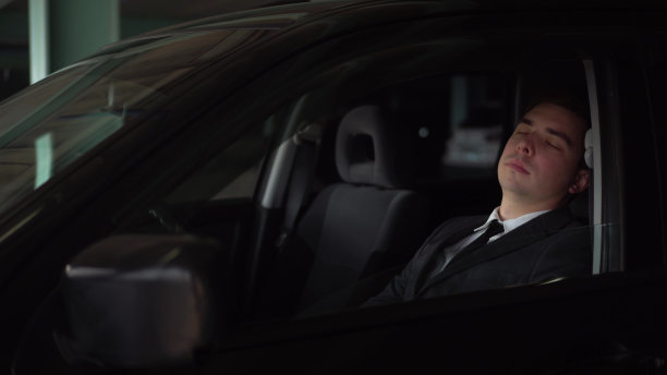 一个穿西装的结实男人在停车场的车里打了个哈欠睡着了。年轻的商人累了，就靠在车里睡觉。图片下载