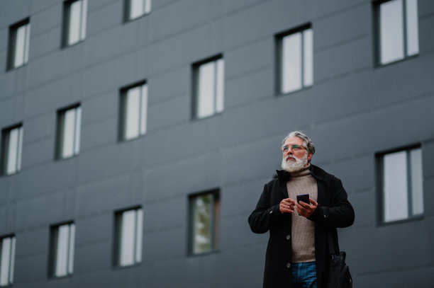 一名高级商人在办公楼外使用智能手机的画像图片下载