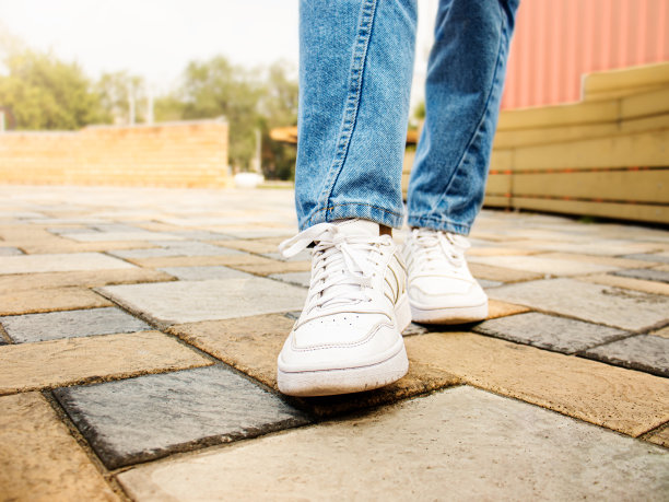 穿着白色运动鞋和牛仔裤的男人或女人在人行道上选择性聚焦图片下载