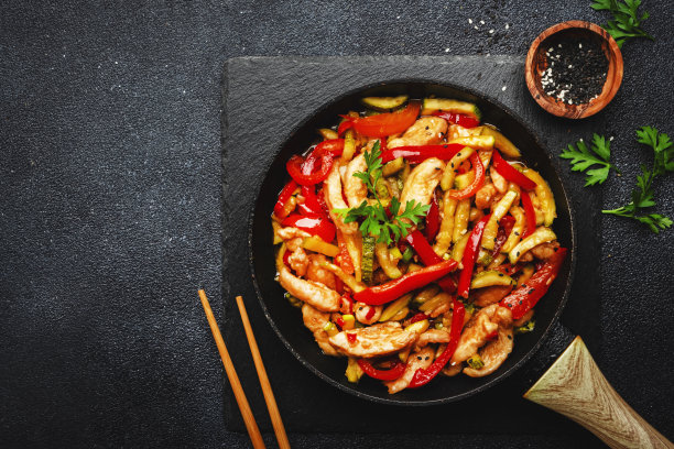亚洲菜，加入鸡肉，红辣椒粉和西葫芦在煎锅里翻炒。黑色厨房桌面背景，俯视图，复制空间图片下载