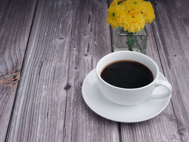 木桌上放着一只白色的咖啡杯，花瓶里插着一朵黄色的花图片下载
