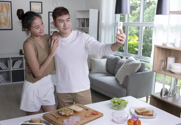 年轻的亚洲夫妇在家里的厨房里做饭和自拍时看起来很开心。图片下载