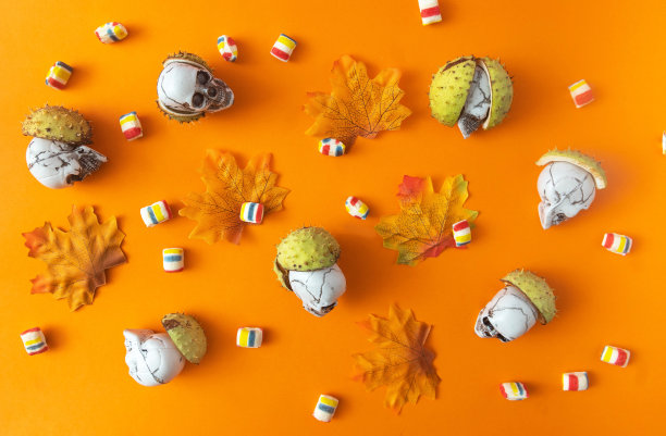 用栗子壳、秋叶和橙色背景下的糖果做成的墙纸。万圣节横幅或卡片或广告的超现实构图或概念。平躺图片下载