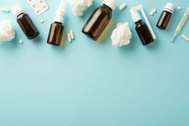 疾病的概念。俯视图照片补救透明棕色喷雾和糖浆瓶水泡包装药片温度计和皱皱的纸餐巾在孤立的浅蓝色背景与空白图片下载