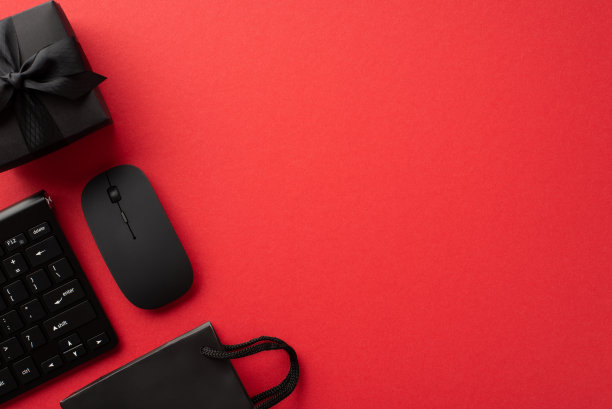 星期一的概念。俯视图照片键盘电脑鼠标黑色礼盒丝带蝴蝶结和纸袋孤立的红色背景与copyspace图片下载