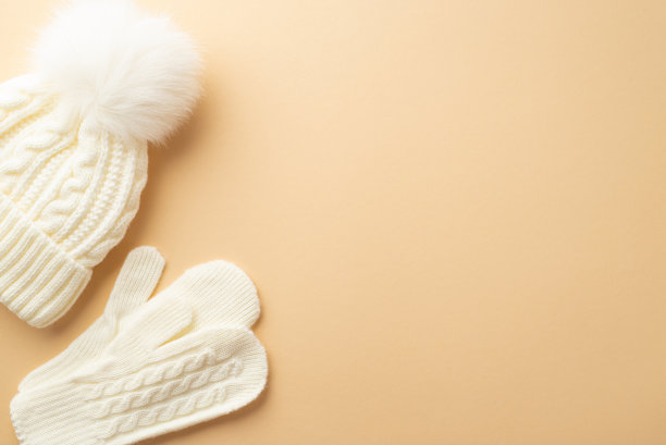 冬天的概念。俯视图照片的白色针织手套和泡泡帽在孤立的米色背景与复制空间图片下载