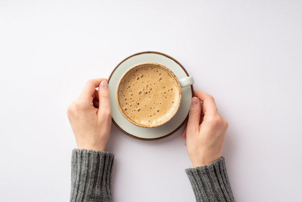 秋天情绪的概念。第一人称俯视图照片的女性手在灰色毛衣拿碟杯泡沫咖啡孤立的白色背景图片下载