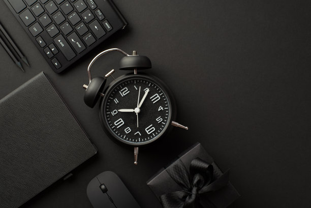 “黑色星期五”的概念。顶视图照片黑色礼盒带蝴蝶结闹钟计划铅笔电脑鼠标和键盘上孤立的黑色背景与copyspace图片下载