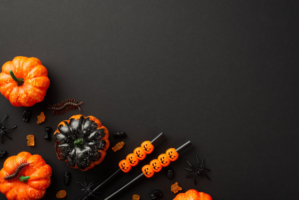 万圣节派对的概念。俯视图照片小南瓜鸡尾酒吸管果冻糖果蜈蚣和蜘蛛在孤立的黑色背景与copyspace图片下载