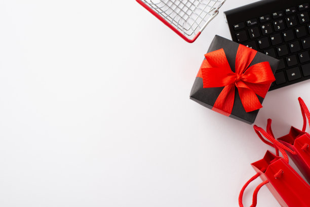 星期一的概念。顶视图照片礼品盒与红色丝带蝴蝶结购物车键盘和纸袋孤立的白色背景与copyspace图片下载