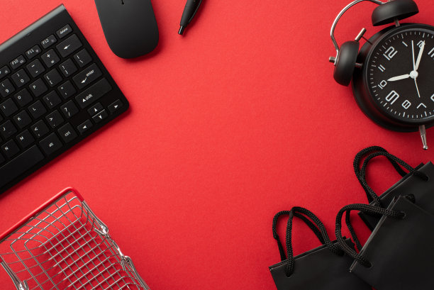 黑色星期五购物概念。俯视图照片黑色闹钟纸袋钢笔购物车电脑鼠标和键盘在孤立的红色背景与中间的copyspace图片下载