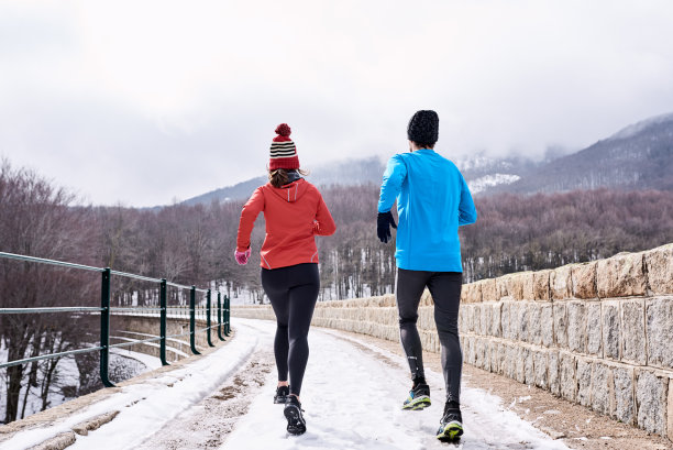一对穿着鲜艳夹克的情侣在山上的水坝上跑步。图片下载