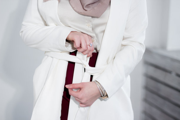 一名戴头巾的穆斯林妇女将腰带系在外套上。白色的夹克。时尚的穆斯林。温柔。穆斯林商人。图片下载