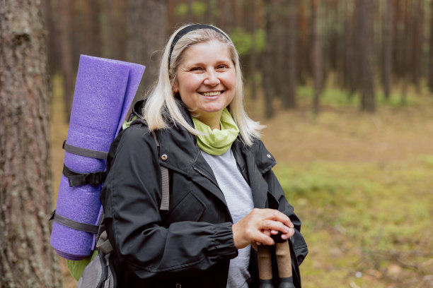 照片中间的特写镜头是快乐的母亲在森林里徒步旅行，拿着徒步杆，垫子和肩膀上的背包图片下载