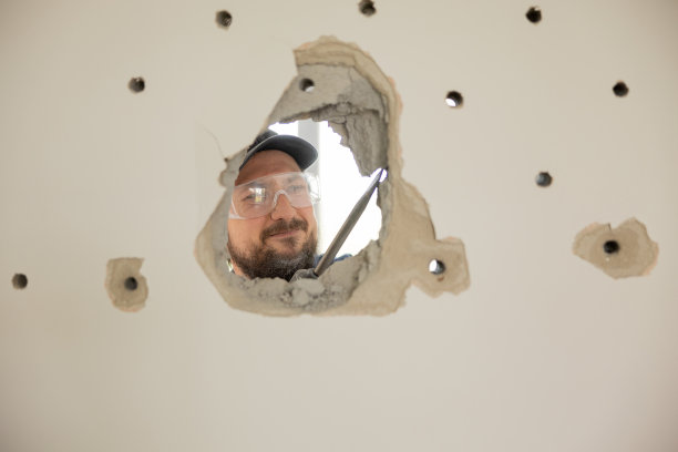 一个人用锤击钻在墙上钻了一个洞。一名戴着护目镜的专注工人继续锻造混凝土水泥图片下载