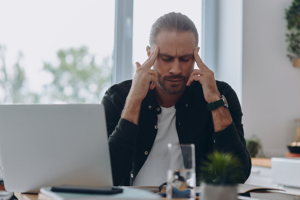 沮丧的年轻人坐在办公室的工作场所用手指按摩头部图片下载